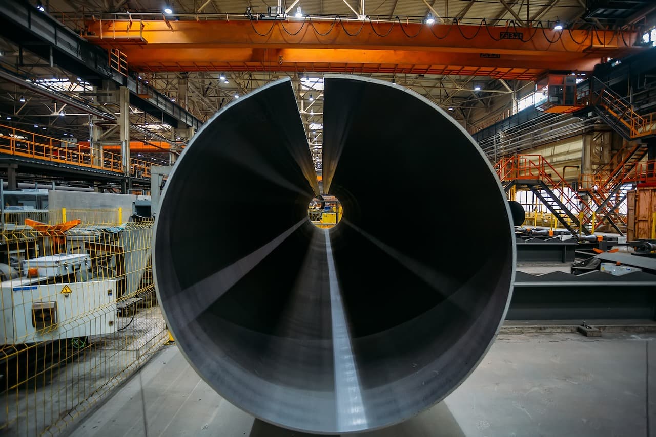 Tubería de acero en un taller industrial con grúas y maquinaria.
